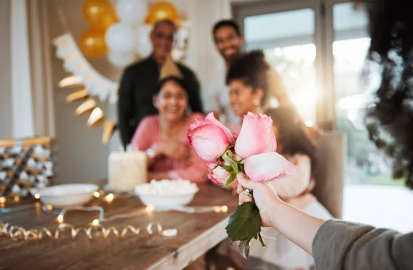 Roses, family and hand with a gift for a celebration at a birthday, mothers day or party in a house. Giving present, love and a child with flowers for women or grandmother to celebrate mothers day.