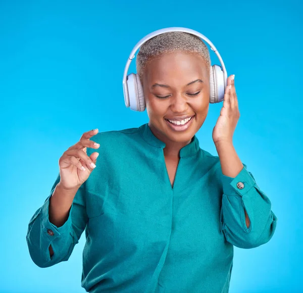 African woman, headphones and studio for listening, music and smile with dancing by blue background. Young gen z student, sound tech and happy for audio streaming, online radio and excited with dance.