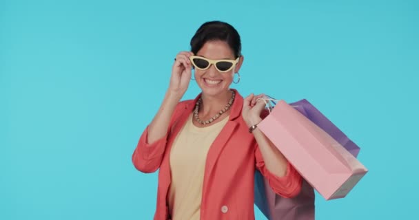 太阳镜 眨眼或快乐女人的脸 戴着蓝色背景的购物袋 穿着时尚或衣服 微笑或富有的女孩 带着打折或促销的产品或礼物 — 图库视频影像