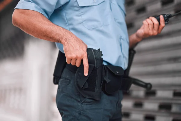 Closeup, law or police officer with a gun, safety or career with legal enforcement, armed or crime. Zoom, man or security guard with service weapon, protection or danger with walkie talkie or uniform.