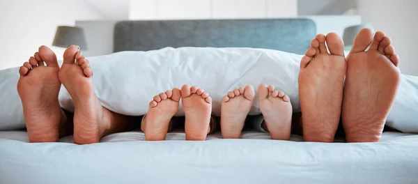 Stock image Family feet, bed and blanket in closeup, parents or kids sleeping on holiday in morning, care and relax. Bedroom, people and sleep with mom, dad or children on vacation, home or break in hospitality.