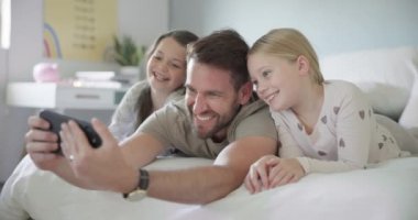 Mutlu, baba ve çocuklarla yüz ve özçekim, kızlar ya da evde aileyle kaliteli zaman geçirmek ya da sosyal medya ve profil fotoğrafı için fotoğraf. Baba, çocuklar sabah telefonda gülümseyip yatakta dinleniyorlar..