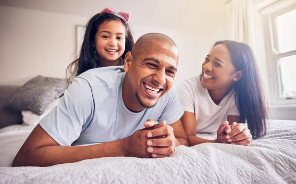 stock image Mother, father and child laughing on a bed in a family home while happy and playing for quality time. Man, woman or parents and girl kid together in the bedroom for morning bonding with love and care.