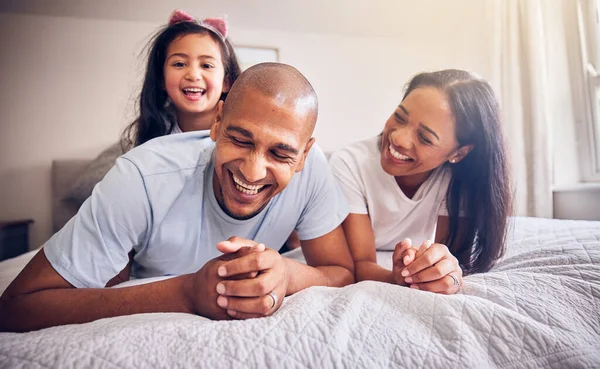 Family, relax and happy on a bed at home while laughing and playing for funny quality time. Man, woman or parents and a girl kid together in the bedroom for morning bonding with love and care.
