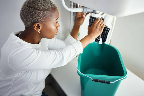 Plumbing, water and a black woman in the bathroom of her home with a cloth and bucket waiting for assistance. Sink, emergency and burst pipe with a young female homeowner in her house to stop a leak.