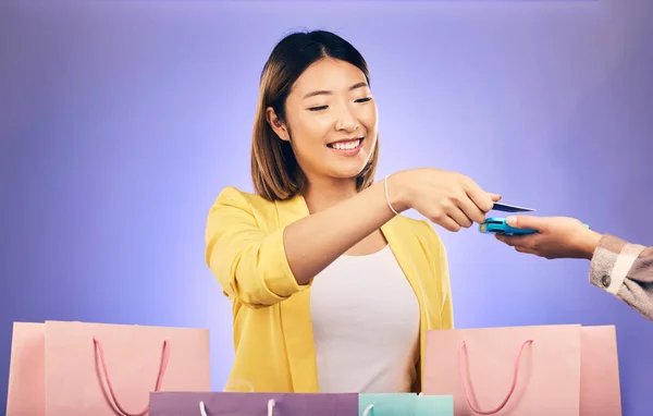 Card machine, shopping bag and woman POS, online payment and digital service or fashion fintech. Retail credit and cashier hands, asian customer or people at point of sale on studio purple background.