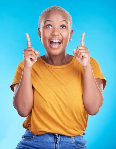 Excited, pointing up and happy black woman with studio advertising space, retail promotion news or announcement. Smile, brand notification and African person gesture at sales deal on blue background.