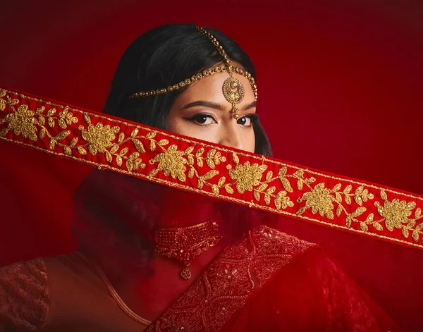 Fashion, culture and portrait of Indian woman with veil in traditional clothes, jewellery and sari. Religion, beauty and eyes of female person on red background with accessory, cosmetics and makeup.