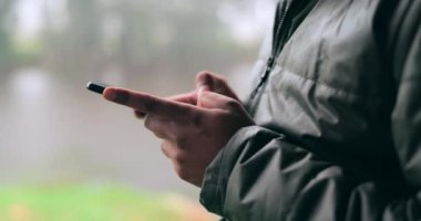 Bulanık arka planda bulutlu bir günde bir insanla eller, telefon ve iletişim. Kışın yağmurda mesaj yazan bir yetişkinle cep telefonu, iletişim ve sosyal medya.