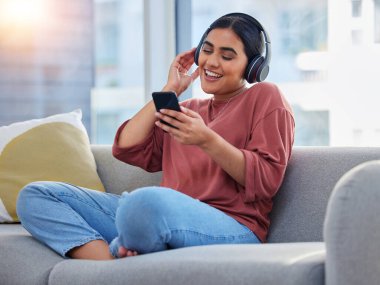 Rahatla, kanepede bir kadınla müzik ve telefon çal ve dans et, sosyal medya ve ses için. Happy, teknoloji ve radyo. Evde müzik ve enerji için kulaklık dinleyen biri var..