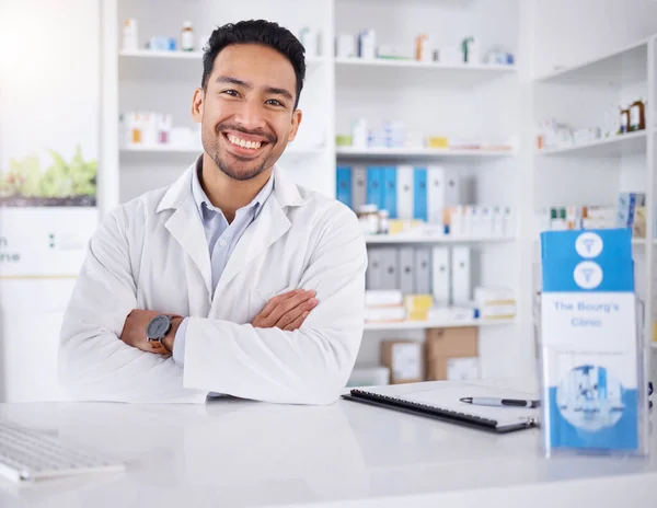 Asian man, portrait and pharmacist with arms crossed in pharmacy, drugstore or shop. Face, confidence or medical professional, happy doctor or worker with a pharmaceutical job for healthcare in Japan.