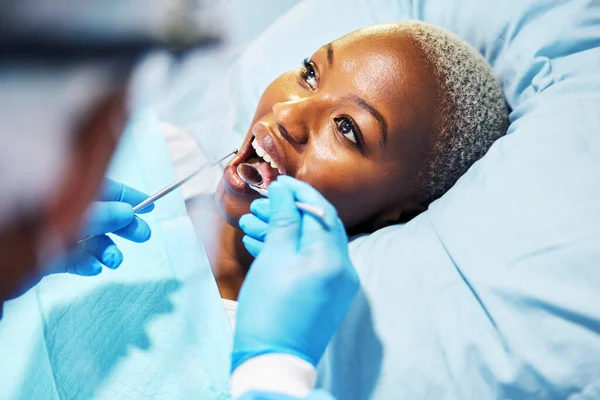 stock image Dentist, inspection and woman with tools in mouth at clinic for cavity, teeth whitening and helping hand for pain. Dental surgeon, African patient and mirror for exam, care or check for healthy smile.