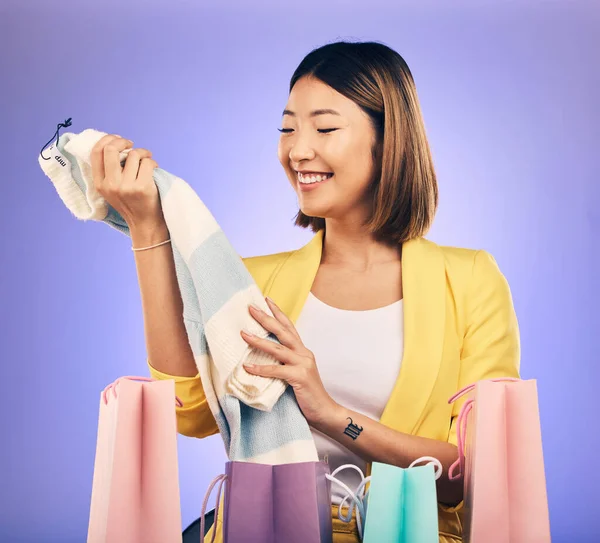 Shopping bag, clothes and woman or customer with product sale, discount or promotion on studio, purple background. Happy young model or asian person with fashion choice, retail and unboxing gift.