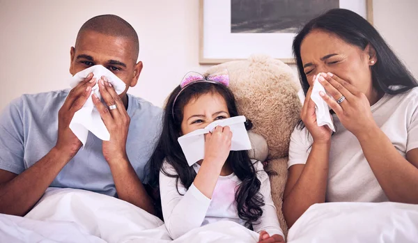 Family, sick and blowing nose on a bed together in a bedroom with allergy or virus and wipe with tissue. Disease, mother and father with kid or child with cold, flu and in winter as parents and girl.