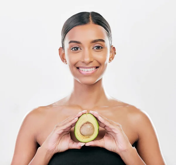 stock image Woman, beauty and avocado in studio portrait for health, wellness and diet for facial glow by white background. Girl, model and healthy skin with fruit, makeup or cosmetics for self care with smile.