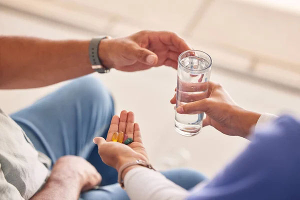 Hands with pills, old man and nurse with water for supplements, support and help at nursing home. Medicine, senior care and caregiver with sick patient, tablet and glass for healthcare in retirement.