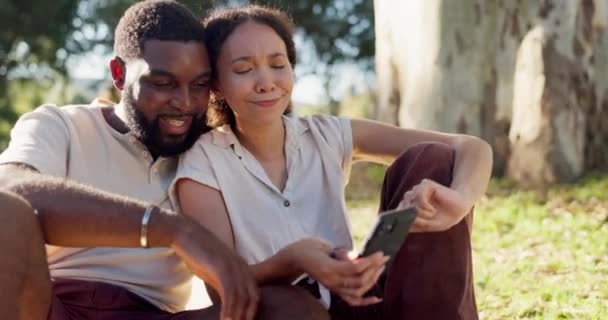 コミュニケーション テクノロジー アプリのための電話でピクニックに笑い ソーシャルメディアと異人種間のカップル 公園でのデートのためのチャットのためのモバイルと話して 夏と黒の男と女 — ストック動画
