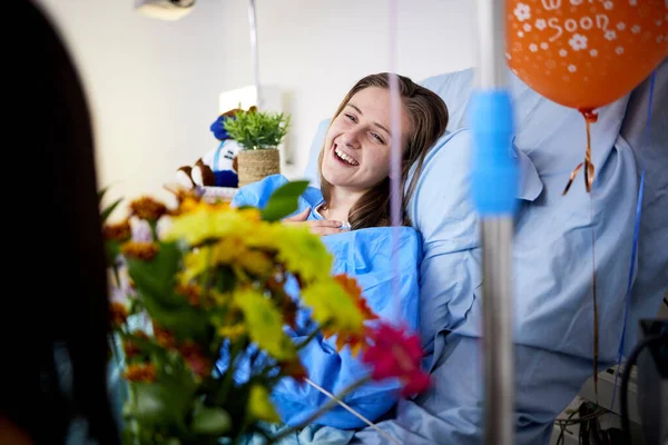 病気の患者と支援を受けて回復中の女性とベッドで花を持つ訪問者 医療保険 花束を持つ人 家族やケアはすぐに気球を取得します — ストック写真