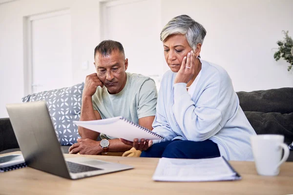 Senior couple, tax documents and stress with laptop in living room for planning, thinking and budget. Elderly man, woman and paperwork for financial compliance, anxiety or debt in retirement on sofa.