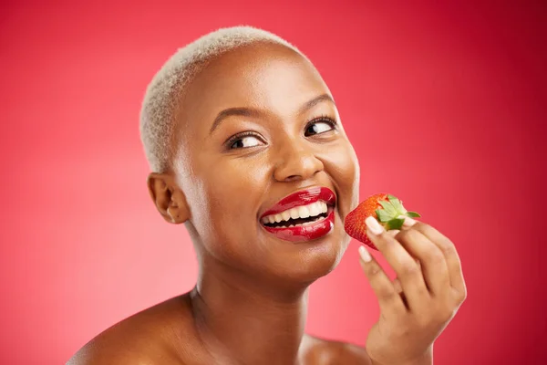 Beauty, thinking face and a woman with a strawberry on a red background for health and wellness. Black female aesthetic model with a smile, makeup and fruit for nutrition and healthy diet in studio.