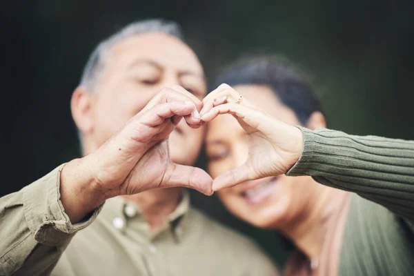 stock image Heart, hands and a senior couple in a house for love, care and showing an emoji together. Happy, trust and an elderly man and woman with a gesture for romance, marriage or valentines day with bokeh.