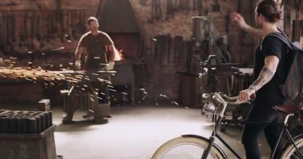 自転車の男と産業金属のワークショップで同僚を迎える 鋼工場での輸送のための自転車を持つ同僚 到着と男性への歓迎のための手のジェスチャー — ストック動画