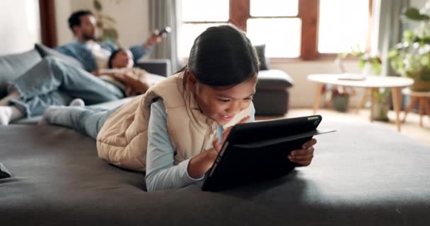 快乐的女孩 平板电脑 在家里客厅的沙发上放松一下 在网上播放动画片或录像 微笑和孩子躺在沙发上滚动社交媒体 游戏应用或浏览互联网 — 图库视频影像