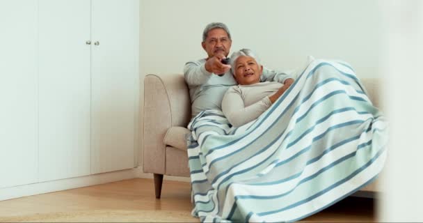 シニアカップルは 映画やショーを指しているための家庭のリビングルームの毛布とソファの上でテレビをリラックスして見てください 女性または幸せな高齢者男とともにテレビリモートのために家のストリーミングオンソファ — ストック動画
