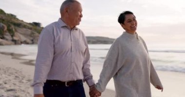Kıdemli çift, aşk, ilgi ve seyahat için gün batımında el ele tutuşup sahilde yürüyorlar. Mutlu erkek ve kadın birlikte gülüyor okyanusta emeklilik tatili için ya da doğada konuşurken..
