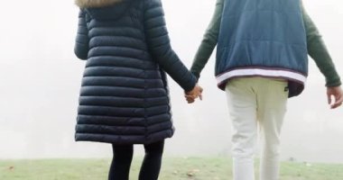 Couple, holding hands and walking in misty fog, travel or adventure together in the nature outdoors. Rear view of man and woman exploring natural environment in winter weather on holiday trip outside.