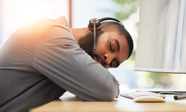Black man, sleeping on desk and tired call center employee, insomnia or mental health problem with headset and mic. Burnout, fatigue and male consultant with stress, nap at work with customer service.