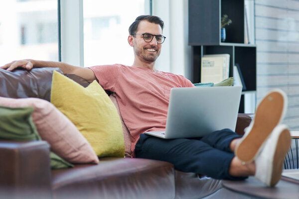 High website traffic makes a happy entrepreneur. Shot of a young man using a laptop while relaxing on a sofa