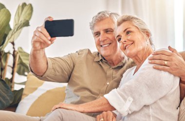Mutlu son sınıf çifti, sarıl ve selfie çek oturma odasındaki kanepede rahatla fotoğraf, anı veya evdeki video bloğu için. Yaşlı adam ve kadın resim, fotoğraf ya da sosyal medya paylaşımı için kanepede birlikte gülümsüyor..
