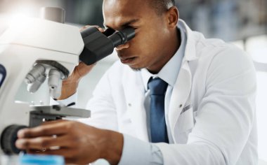 Yakından bakınca laboratuvarında araştırma yaparken mikroskop kullanan yakışıklı genç bir bilim adamının kesilmiş portresi.