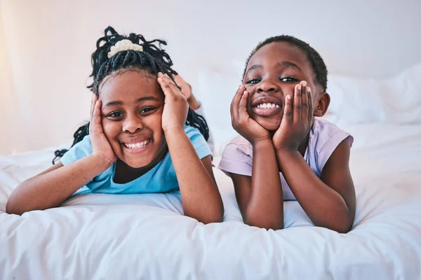 Happy, relax and portrait of children on the bed for playing, bonding and quality time in the morning. Cute, smile and little African kids or siblings in the bedroom of a house for childhood together.