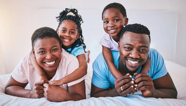 Happy, black family and portrait in a bed with smile, care and comfort on the weekend in their home. Face, love and children with parents in bedroom playing, hug and relax in the morning together.