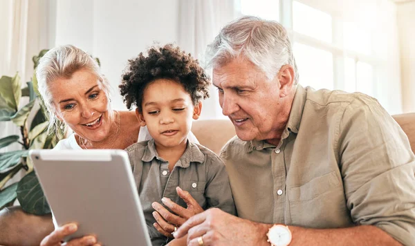 Family, grandparents and child on tablet in home e learning, online education and watch or streaming cartoon. Happy interracial kid and senior people on digital technology for teaching school on sofa.