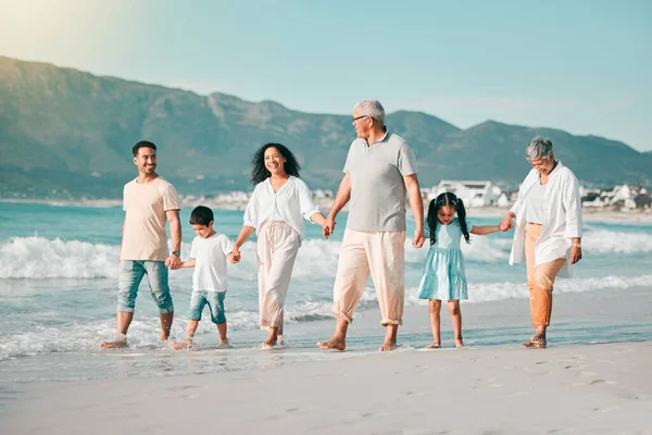 Generations, holding hands and walking family on beach and ocean waves, freedom and bonding in nature. Grandparents, parents and kids, people outdoor and travel with trust and love on Mexican holiday.