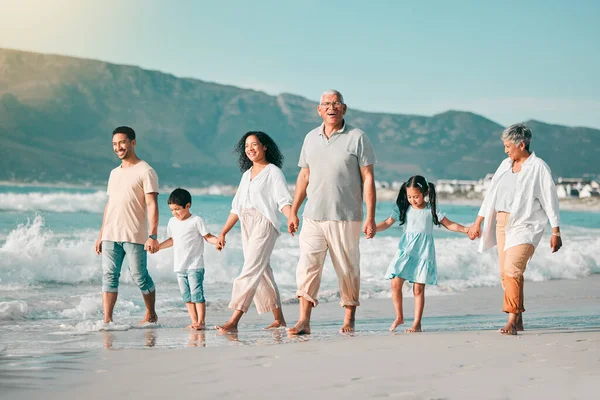 Holding hands, family is walking on beach and ocean, generations and bonding in nature with waves. Grandparents, parents and kids, people outdoor and travel with trust and love on Mexican holiday.