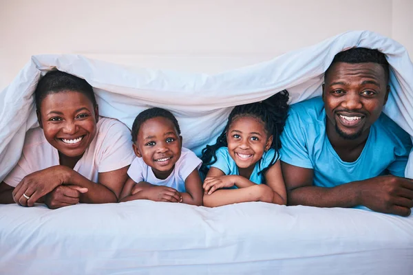 Happy, black family and portrait in a bed with blanket, relax and comfort on the weekend in their home. Face, smile and children with parents in bedroom playing, cover in the morning with fun.