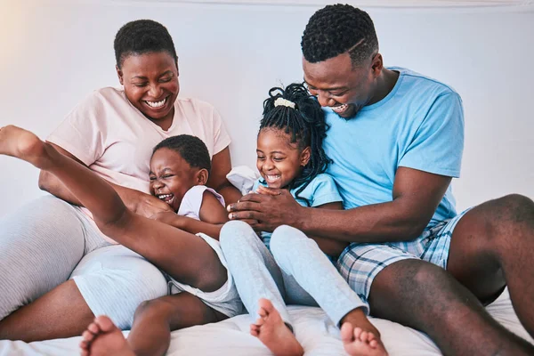 Laugh, black family and tickle in a bed with smile, care and happy on the weekend in their home. People, playing and children with parents in bedroom with games and having fun in the morning together.
