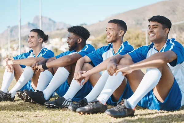 Happy soccer players, relax or team on a field for a sports game together in summer on resting break. Smile, stadium or group of football athletes sitting after fitness exercise, training or match.
