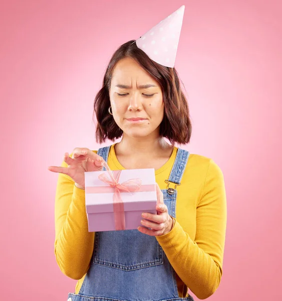 Birthday present, studio box and Asian woman stress over package, ribbon opening fail or party event. Problem, bad gift mistake and Japanese person with doubt, unsure or sad on pink background.