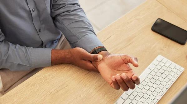 Hand, wrist pain and a business black man at his desk in the office with an injury while working on a keyboard. Arthritis, injury or carpal tunnel with an employee sitting at his workplace from above.