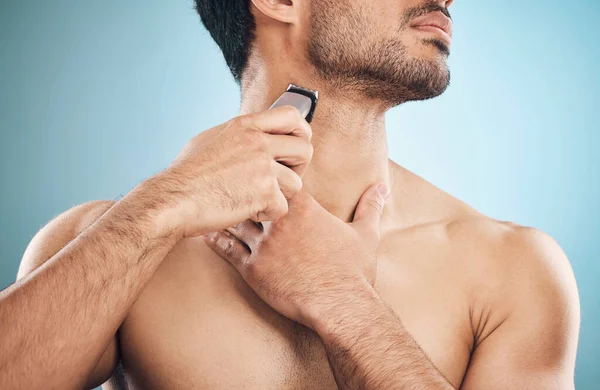 Hands, shaving and electric razor with a man in studio on a blue background for personal hygiene or grooming. Beauty, wellness and cosmetics with a young male in the bathroom for hair removal.