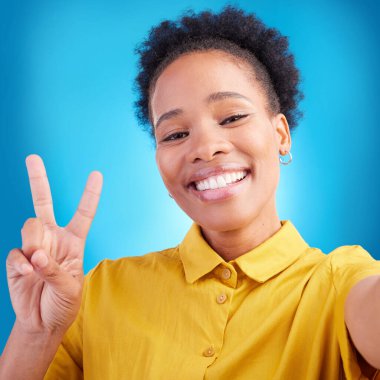 Mutlu kadın, portre gülüşü ve selfie için barış işareti, fotoğrafçılık ya da mavi bir stüdyo geçmişine karşı hafıza. Fotoğraf, fotoğraf veya çevrimiçi sosyal medya paylaşımı için Afrikalı kadın ya da fotoğrafçı.