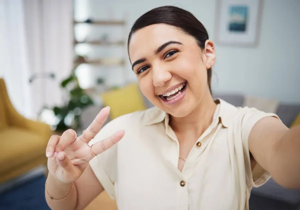 Face of woman, portrait and peace for selfie in home, video call and live streaming vlog in living room. Happy young gen z girl show v sign, hand emoji and memory for profile picture on social media.
