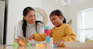Anne, evdeki çocuk gelişimi için kız çocuğuyla mutfakta yapı taşlarıyla oynuyor. Mutlu, kaynaşmış ve genç Asyalı anne evinde eğlenmek için kızına tahta oyuncaklarla yardım ediyor.