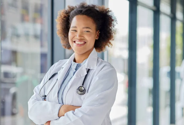 Happy black woman, portrait and doctor with arms crossed in clinic for wellness services, help or medical consulting. Medicine, healthcare and young female professional working with trust in hospital.