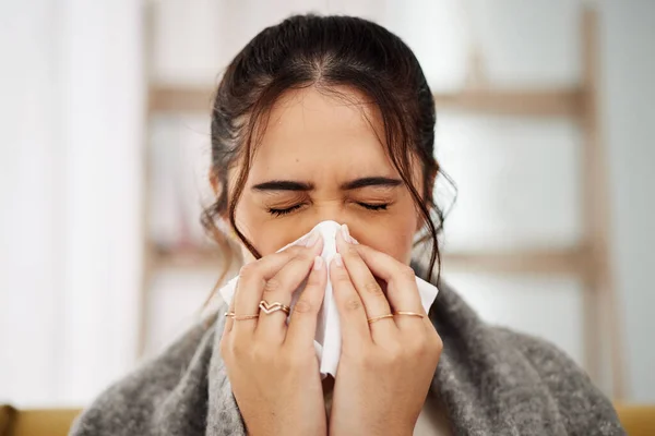 Tissue, nose and sick woman sneezing in living room with allergy, cold or flu in her home. Hay fever, sinusitis and female with viral infection, risk or health crisis in lounge with congestion.